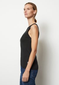 Top negru fără mâneci, cu un design adaptat, decolteu rotund și textură netedă, asociat cu blugi din denim albastru cu croială dreaptă.