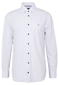 Camicia bianca con bottoni, decorata con piccoli pois neri, maniche lunghe, colletto classico e bottoni scuri. Presenta un accento con logo discreto. Texture liscia.