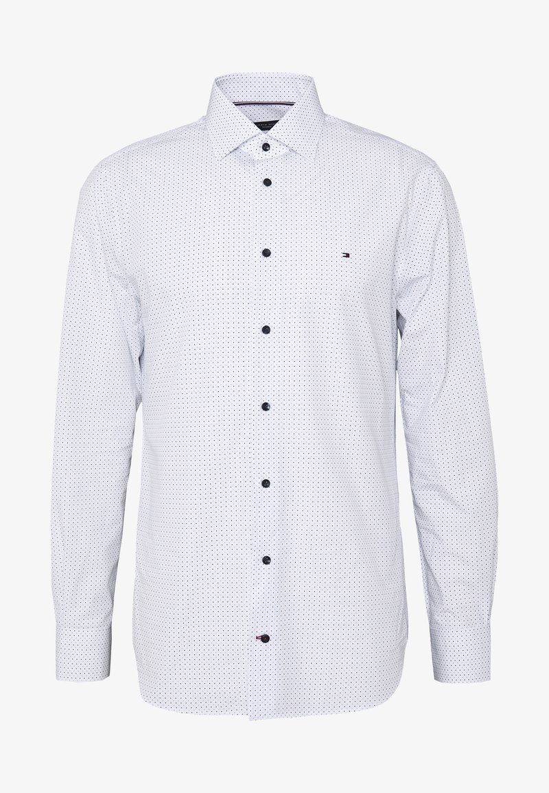 Camicia bianca con bottoni, decorata con piccoli pois neri, maniche lunghe, colletto classico e bottoni scuri. Presenta un accento con logo discreto. Texture liscia.