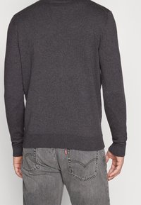 Mörkgrå stickad tröja med långa ärmar, ribbade manschetter och fåll. Bärs med blekta grå jeans med en igenkännlig logotyp på baksidan.