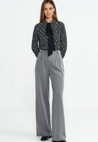 Czarno-biała bluzka w pionowe paski z kołnierzem wiązanym na kokardę, połączona z wysokim stanem szarymi spodniami o szerokich nogawkach i gładkiej fakturze.