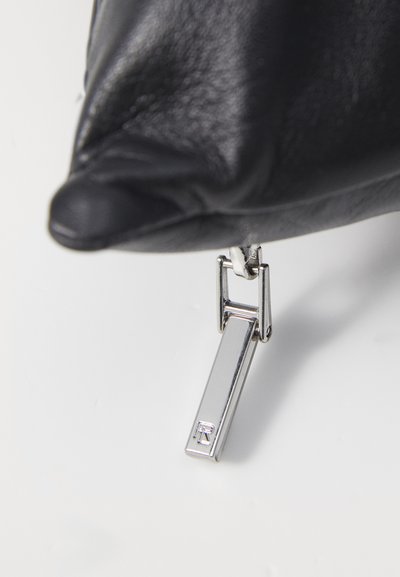 Čierny kožený púč s hladkým povrchom, ktorý má strieborný zips s obdĺžnikovým tvarom a vystúpeným logom.