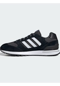 Baskets noires de sport avec une tige en suède et en maille, présentant trois rayures blanches, un col rembourré et une semelle intermédiaire blanche avec une semelle extérieure en caoutchouc texturé.