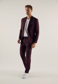 Burgundy suit with a tailored fit, paired with a white t-shirt and white sneakers. Simple jacket design, smooth fabric, subtle pocket detail.