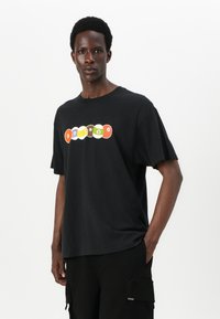 Black cotton t-shirt featuring a colorful graphic of circular designs in red, orange, brown, green, and purple across the chest.