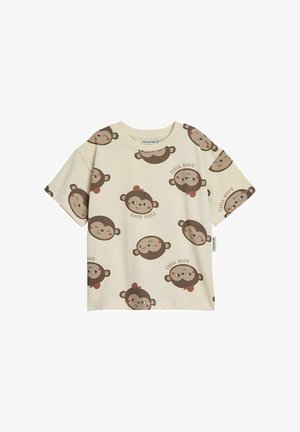 Beige t-shirt met een herhaald print van een aap-gezicht in bruin met rode accenten, en de tekst "GOOD VIBES" in een speelse lettertype.