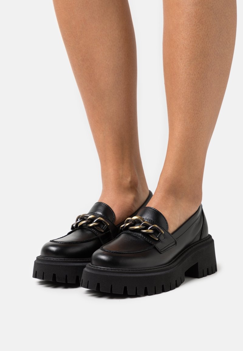 Mocassins en cuir noir avec une semelle épaisse et côtelée, ornés d'une chaîne dorée décorative sur le dessus pour un détail supplémentaire.