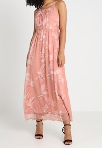 Maxiklänning i ljusrosa chiffon med blommönster. Har spaghettistroppar, samlad midja och slits på sidan. Mjuk, flödande textur.