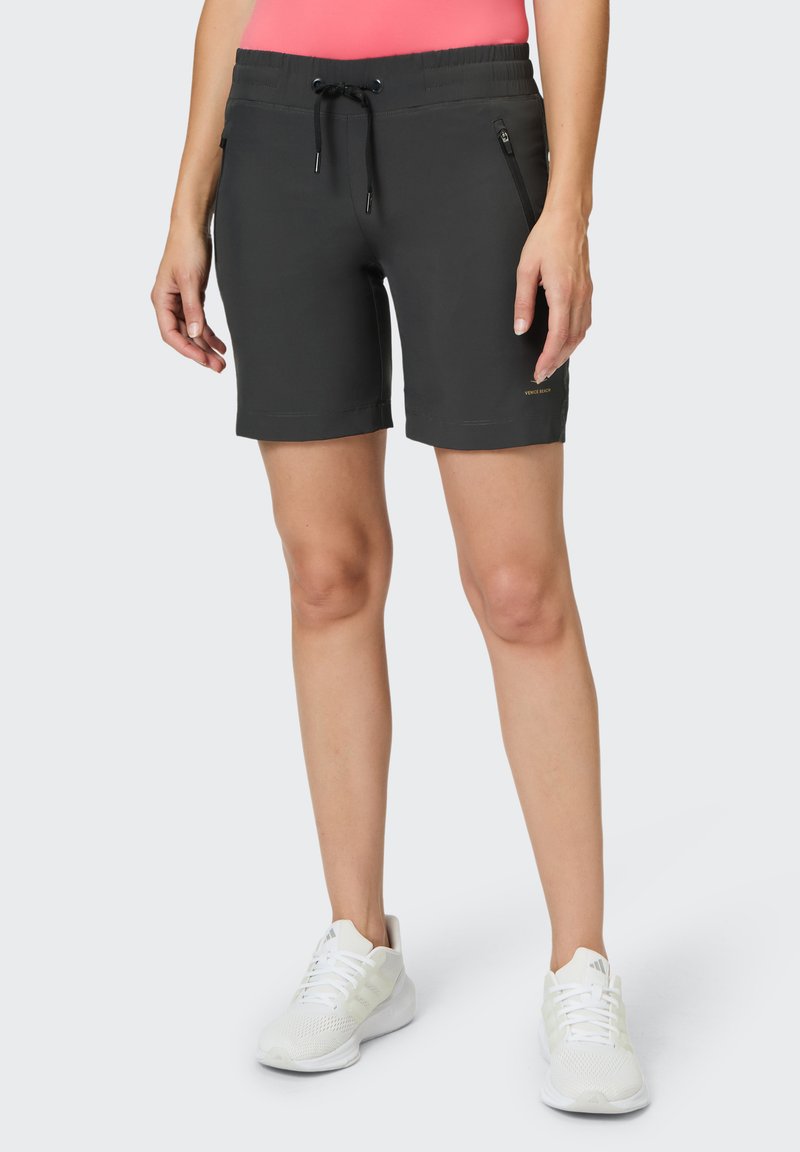 Graue Shorts mit elastischem Bund und Kordelzug; mit zwei Reißverschlusstaschen. Kombiniert mit weißen Sportschuhen.