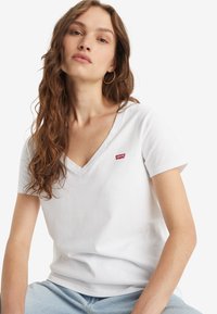 Bijela pamučna majica s v-neck izrezom i kratkim rukavima. Sadrži mali crveni Levi's logo na prsima. Mekan materijal, ležeran kroj.