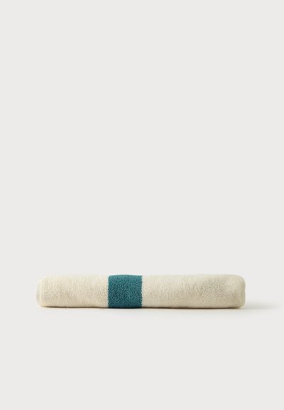 Serviette crème roulée avec une large bande bleu sarcelle au centre, posée sur une surface claire et plate.