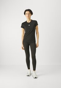 Top atlético negro de manga corta con logotipo blanco, combinado con mallas negras y zapatillas blancas. Tela suave, diseño ajustado.