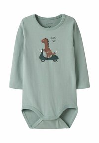 Jasnozielona, długa rękawiczka dla niemowląt z grafiką dinozaura jeżdżącego na hulajnodze oraz napisem "LECIMY!" na klatce piersiowej, z zatrzaskami na dole.