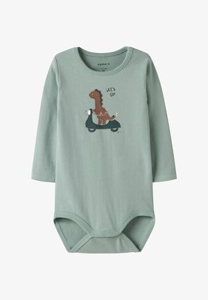 Jasnozielona, długa rękawiczka dla niemowląt z grafiką dinozaura jeżdżącego na hulajnodze oraz napisem "LECIMY!" na klatce piersiowej, z zatrzaskami na dole.