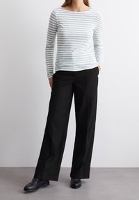 Camicia a maniche lunghe a righe in blu chiaro e bianco, abbinata a pantaloni larghi neri. Tessuto testurizzato e vestibilità rilassata con scollatura a barca.