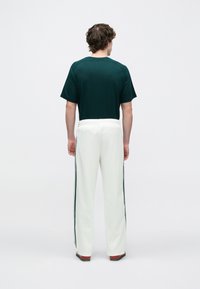 Πράσινο βαμβακερό μπλουζάκι και λευκή φόρμα με πράσινες ρίγες στο πλάι, ελαστική μέση, λεία υφή και άνετη εφαρμογή. Πλάγια όψη πίσω.