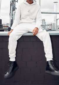 Ljusgrå hoodie och matchande joggers av mjukt tyg, med en logotyp och svarta stjärndetaljer på byxorna. Svarta högskaftade kängor fulländar looken.