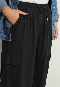 Svarta lätta byxor med elastisk midja, justerbar snörning, sidofickor och mjuk textur, kompletterade med en denimjacka.