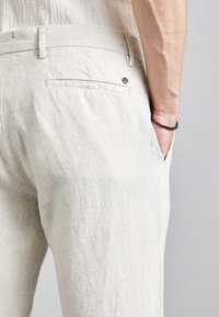 Jasnobeżowe lniane spodnie o fakturowanej powierzchni, z tylną kieszenią i małym czarnym guzikiem z logo.