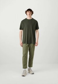 Olivgrünes T-Shirt mit kurzen Ärmeln, olivfarbene Hose, weiße Mütze und beigefarbene Sneakers. Baumwollstoff, lockere Passform, minimalistisches Design und keine sichtbaren Muster.