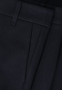 Gros plan sur une ceinture en tissu noir avec passant de ceinture et détail de couture plissée sur un vêtement.