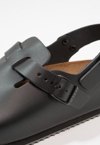 Sandal in pelle nera con finitura testurizzata, cinturino regolabile e soletta in sughero marrone. Fibbia di metallo distintiva. Design aperto a profilo basso.