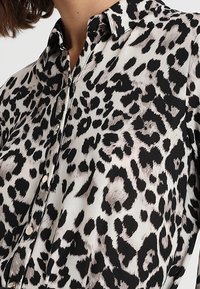Leopard print blouse with a light background, black and brown spots, button-up front, and a classic collar. Soft, smooth fabric texture.