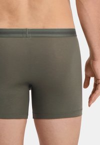 Olajzöld boxeralsó, puha, sima textúrával és kontrasztos sötétzöld csíkos derékrésszel. Szűkített fazon, minimális részletezéssel.