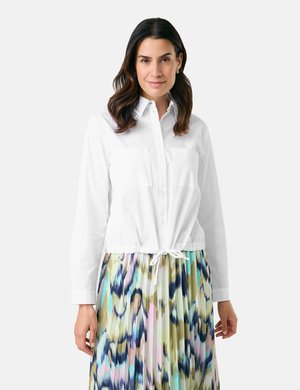 White button-up shirt with long sleeves and two chest pockets, paired with a colorful, pleated, patterned skirt featuring greens, blues, and pinks.
