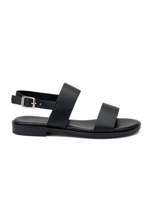 Sandales en cuir noir avec deux larges brides et une bride arrière au niveau de la cheville ornée d'une boucle en argent. Semelle plate au design minimaliste.