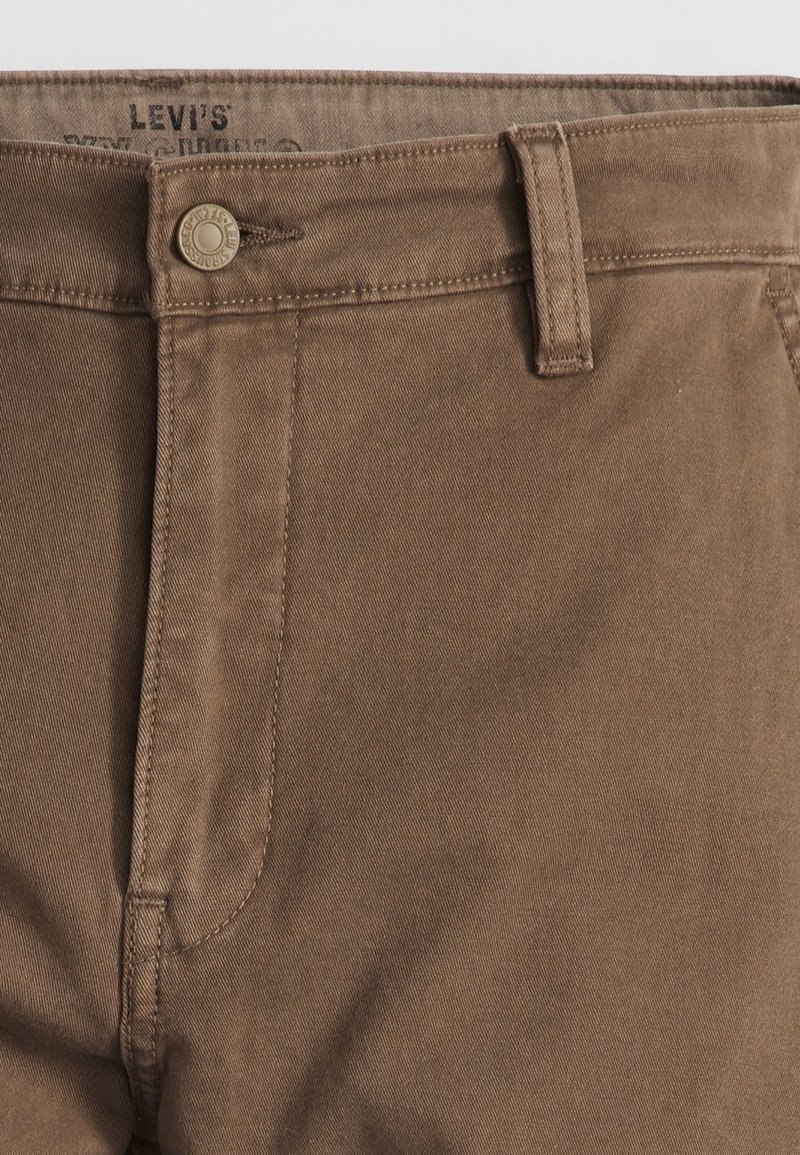 Pantalon en coton marron avec une texture lisse, présentant une fermeture à bouton sur le devant, des passants de ceinture et des détails cousus le long des coutures.