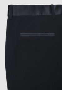 Schwarze maßgeschneiderte Hosen mit einem Satinhochbund und einer dezenten Textur. Verfügt über eine diskrete Gesäßtasche mit einem passenden Satinbesatz.