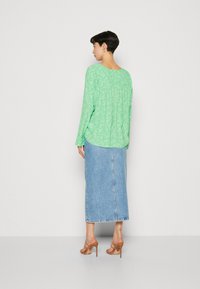 Grønn bluse med blomsterdesign og lange ermer, med plisseringer bak, kombinert med en denim maxiskjørt og nude høyhelte sandaler.