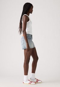 Denim mini-jurk, lichtblauw, vijf-pocket ontwerp, gestikte naden. Witte tanktop, rode en witte sneakers met patroonaccenten.