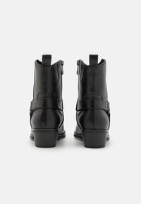 Bottines en cuir noir avec une texture lisse, dotées d'une fermeture éclair latérale, de détails en sangle et d'un talon empilé.
