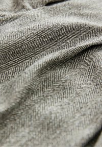 Tissu gris avec un motif chevron tissé, montrant des plis doux et la texture en gros plan.