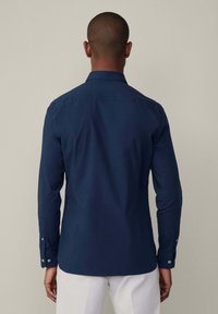 Camisa de manga larga azul marino, hecha de una tela suave, con cuello abotonado, botones en los puños y un diseño ajustado.