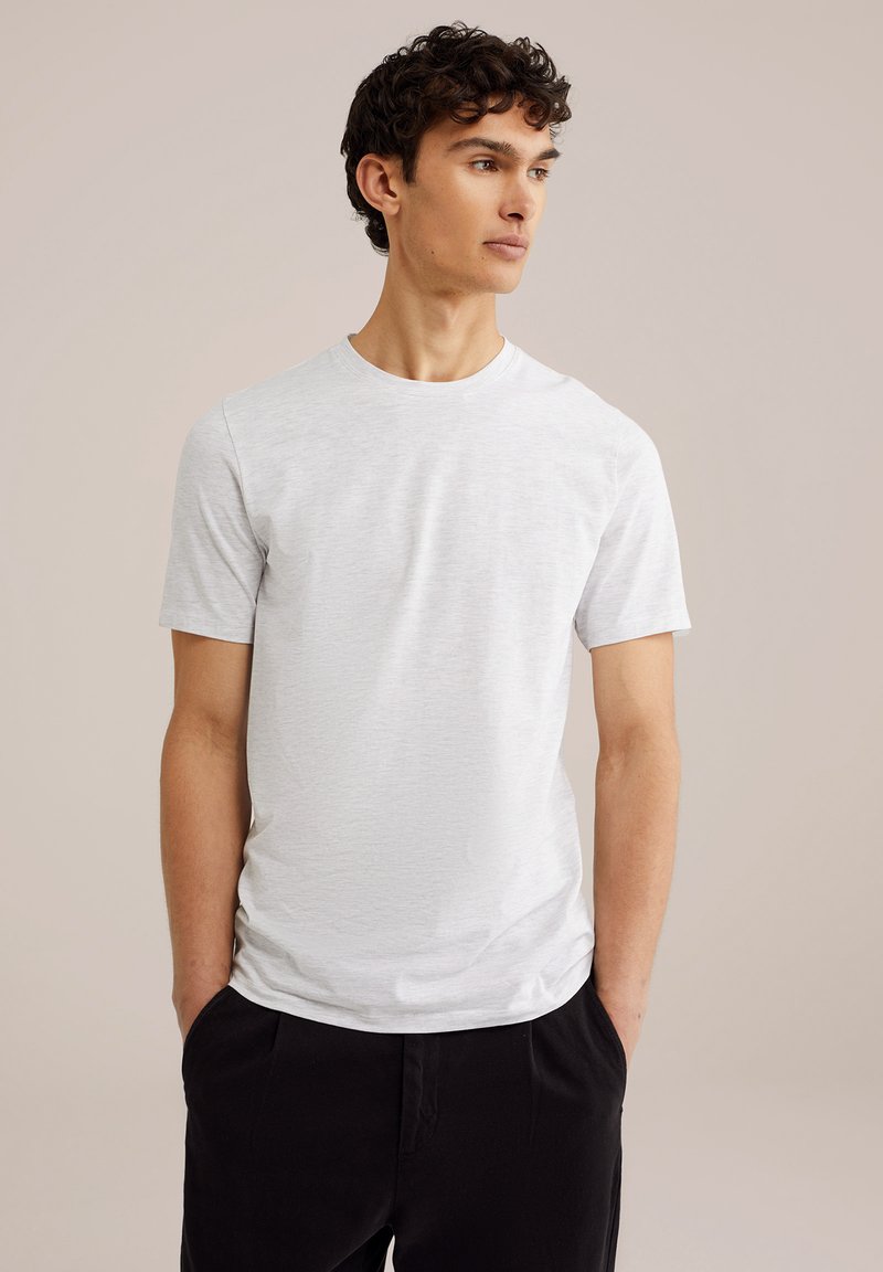 Camiseta de manga corta gris claro hecha de una suave tela texturada con un cuello redondo, combinada con pantalones negros, exhibida sobre un fondo neutro.