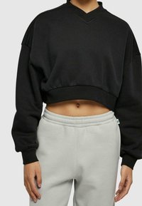 Felpa nera corta con scollo a V e spalle scese, abbinata a pantaloni della tuta grigi chiari con vita elasticizzata. Tessuto morbido.