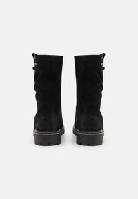 Bottes noires jusqu'au genou en suède, avec un design légèrement plié, un talon renforcé et des coutures légères le long de la semelle pour un détail supplémentaire.