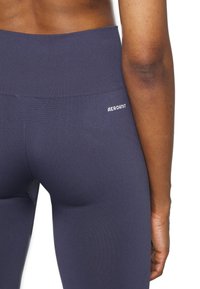 Granatowe legginsy z wysokim stanem, wykonane z gładkiego, elastycznego materiału. Z tyłu znajduje się małe białe logo „AEROKNIT”.