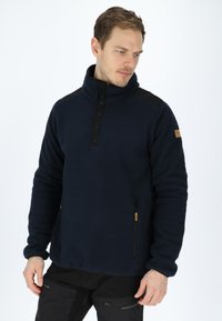 Pullover in pile navy con dettagli neri sulle spalle, chiusura con zip a metà e tasca laterale con zip; presenta una superficie morbida e texture.
