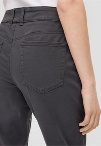 Pantalons en denim gris foncé avec une taille haute, dotés de deux poches arrière et de détails de couture subtils. La texture semble lisse et ajustée.