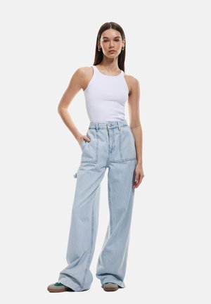 Jeans de pierna ancha de color azul claro con una cintura alta, bolsillos frontales y costuras visibles, combinados con una camiseta sin mangas blanca ajustada.