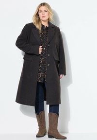 Bruin, gestructureerd wollen jasje met een geknipt kraag, drie knopen en voorzakken, gedragen over een leopardenprint shirt en blauwe spijkerbroek.