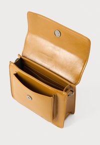 Sac bandoulière en cuir tan avec une texture lisse, fermeture à pression magnétique et plusieurs compartiments pour l'organisation.