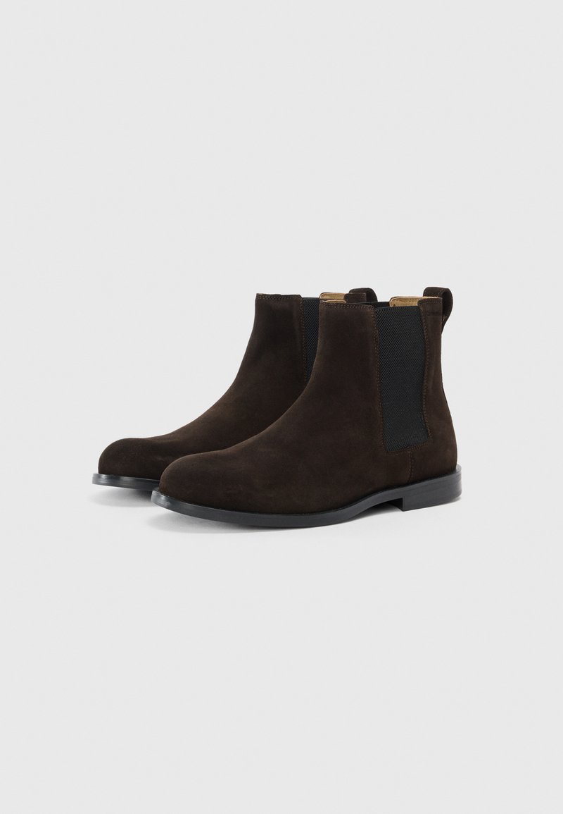 Braune Wildlederschuhe im Chelsea-Stil mit glatter Oberfläche, elastischen Seitenpaneelen und einer niedrigen schwarzen Gummisohle. Verfügt über eine Zuglasche für ein einfaches Anziehen.