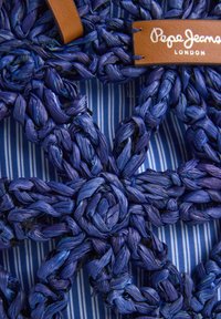 Plava tkanina s tkanim uzorkom stvara teksturirani cvjetni dizajn, upotpunjen smeškim kožnim tagom s natpisom "Pepe Jeans London" u bijelom.