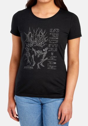 Person trägt ein schwarzes T-Shirt mit grauer Spider-Man-Grafik, hockt und hat Spinnennetz-Designs, kombiniert mit hellblauen Jeans.