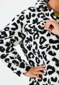 Sort og hvid leopardprint fleecejakke med krave, knaplommer og tekstureret stof. Nærbillede af brystområdet.